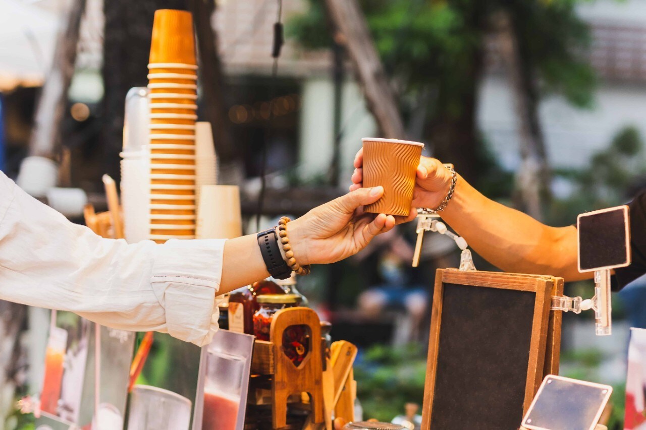 A barista serving a cup of hot coffee to a customer outdoors. A barista serving a cup of hot coffee to a customer outdoors.