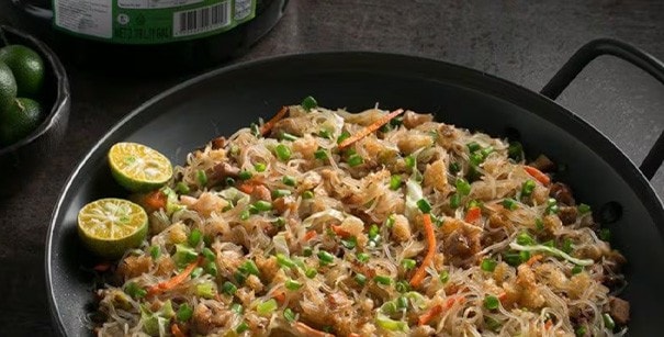 Pancit sisig in a cast-iron pot served with calamansi.