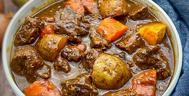 Beef mechado with carrots and potatoes in a white bowl. 