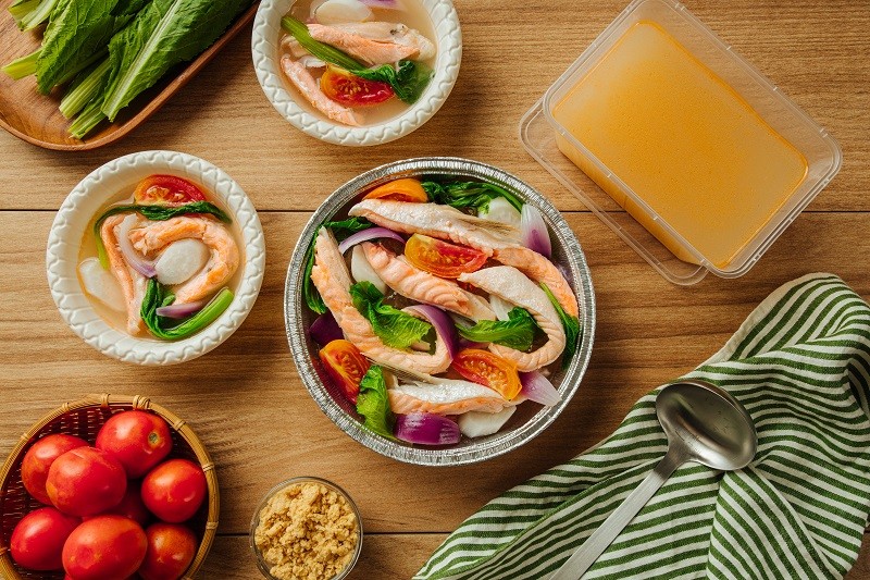 One foil packaging containing sinigang na salmon belly components and a plastic container filled with soup One foil packaging containing sinigang na salmon belly components and a plastic container filled with soup