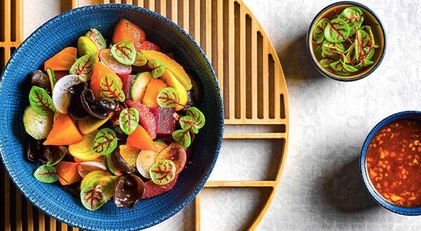A bowl filled with beets, black fungus, citrus fruits, and microgreens with a garlic-based dressing on the side. A bowl filled with beets, black fungus, citrus fruits, and microgreens with a garlic-based dressing on the side.