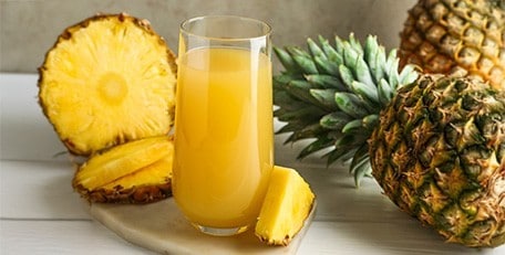 Freshly squeezed pineapple juice in a clear glass on a white kitchen counter.