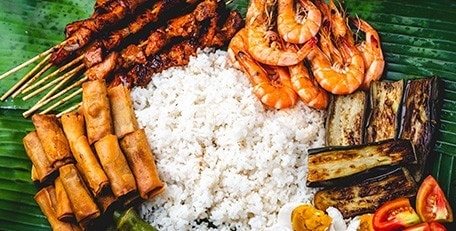 Food for boodle fight, including lumpiang shanghai, barbeque, shrimp, and vegetables.