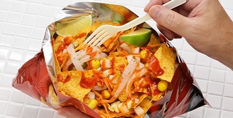 A hand holding a fork taking food from nachos in a bag.