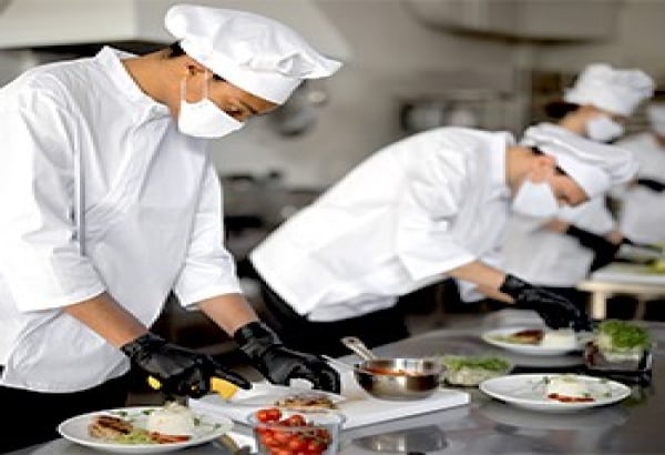 Cooks wearing masks while preparing food in a kitchen. 
