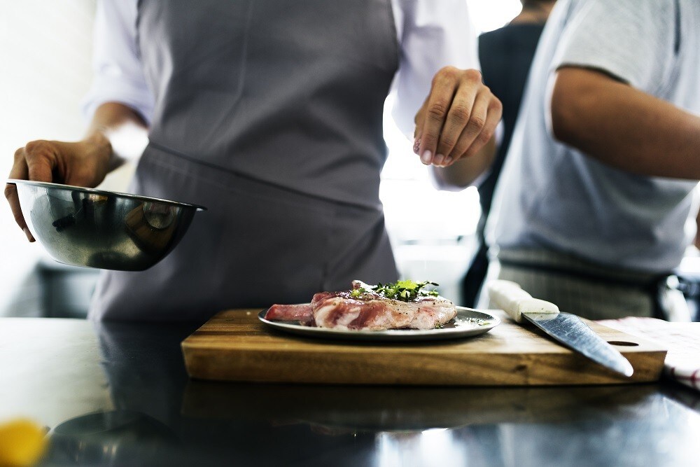 A chef drizzles seasoning and garnishes on a meat dish before serving A chef drizzles seasoning and garnishes on a meat dish before serving
