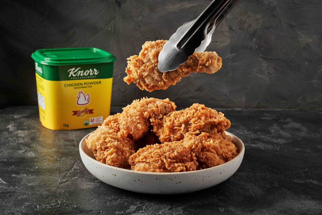 A serving of golden brown fried chicken with Knorr Chicken Powder tub in the background A serving of golden brown fried chicken with Knorr Chicken Powder tub in the background