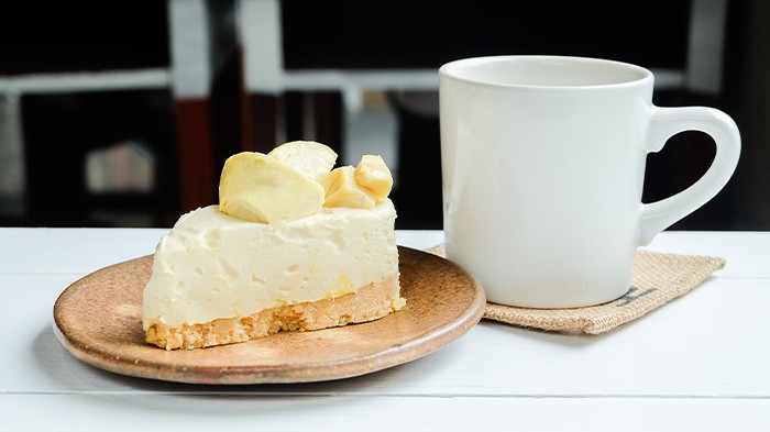 A slice of durian cheesecake on a plate beside a mug.