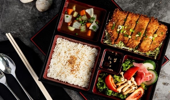 A Japanese-style lunch box with rice, fried fish, vegetables, and soup. A Japanese-style lunch box with rice, fried fish, vegetables, and soup.