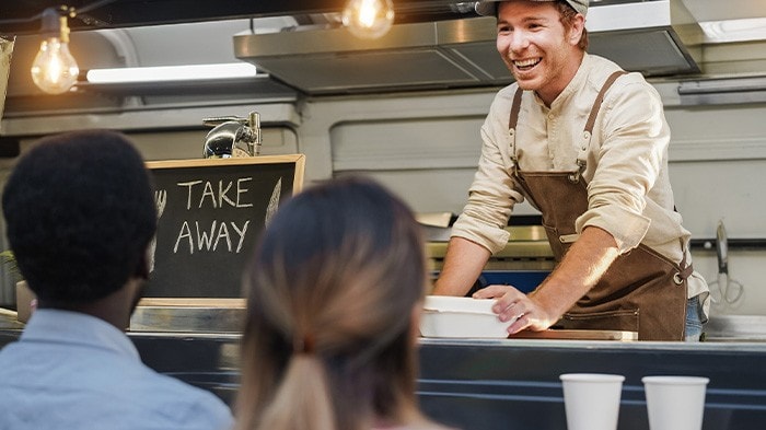 Smiling food truck vendor serving takeaway meals to customers.