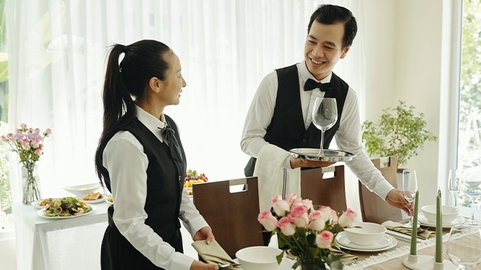 Two Asian waiters setting an elegant table for a formal dining function.
