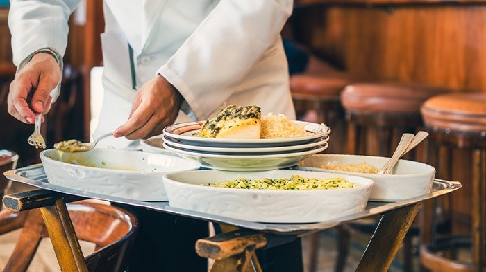 Waiter serving food from a trolley with dishes on plates, showing classic French food and beverage service.