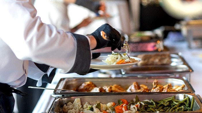 Catering staff serving food from buffet trays, showing buffet style of service.