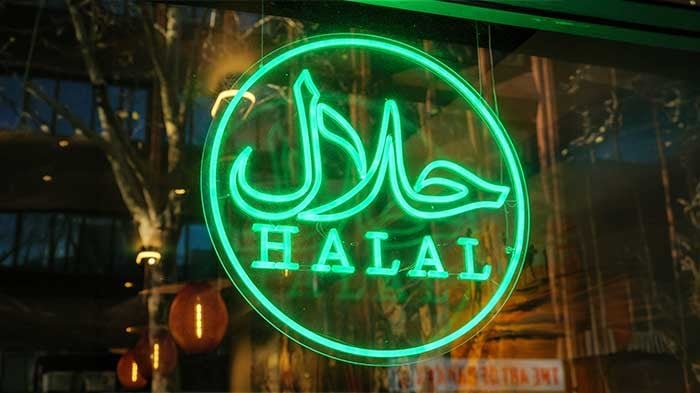 A store’s neon halal sign hanging on a glass wall. 